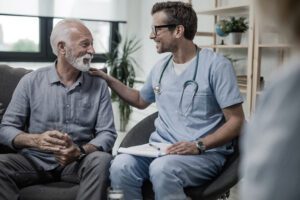 Happy doctor talking to senior male patient while being in a home visit.