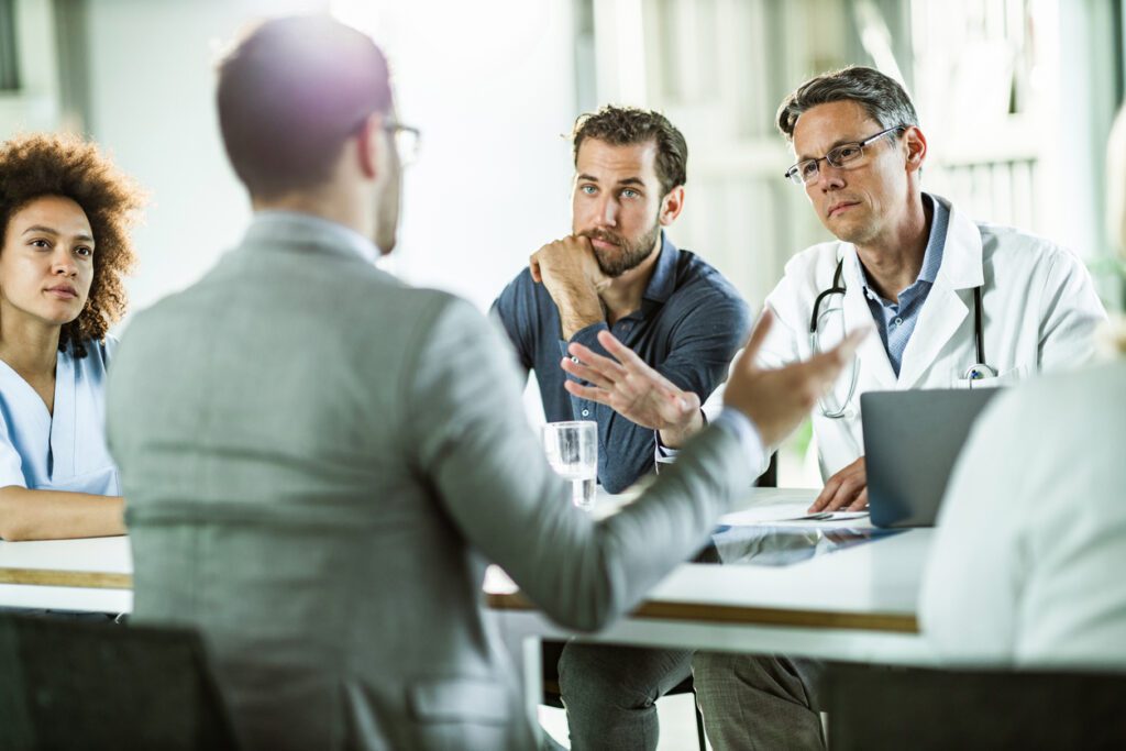 Mid adult doctor talking to businessman during a meeting with their colleagues in the office.