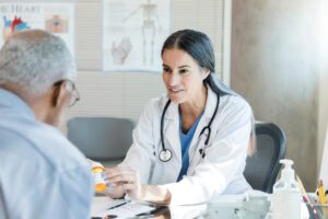 A female doctor discusses with a senior male patient his prescription medication's dosage instructions and side effects. The doctor is showing the patient the label on the medication.