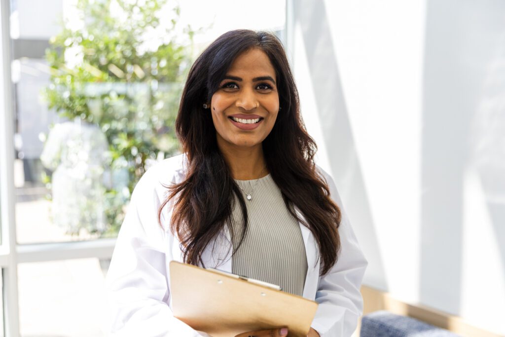 While passing through the atrium of the hospital, the successful mid adult female doctor smiles for the camera to have her photo taken.