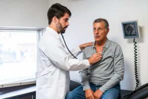 A mature Caucasian man is examined by a young Latino doctor in a medical office setting, depicting a healthcare consultation with focus on patient care.