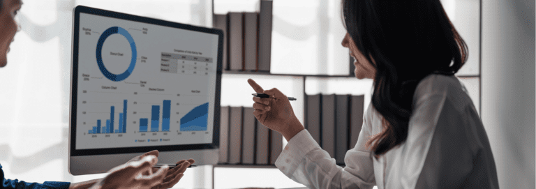 Woman talking to colleague and pointing at computer screen containing charts and graphs|||||||||